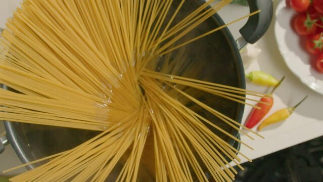 Hand of man putting a bunch of spaghetti into a cooking pot with boiling water while preparing Italian pasta at home. Close-up top down shot