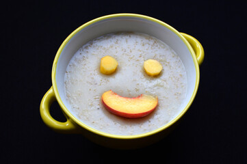 oatmeal and slices of fresh peach in the shape of a smile on a black background. tasty, wholesome and healthy breakfast food for children and adults. proper nutrition for diet