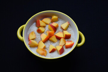 oatmeal and slices of fresh peach in a bowl on a black background. tasty, wholesome and healthy breakfast food for children and adults. proper nutrition for diet