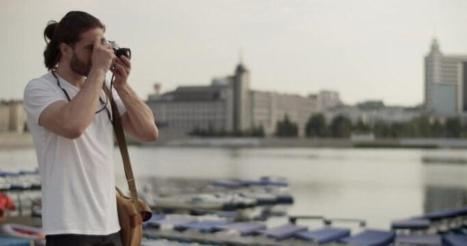 Male tourist standing near river and taking photos on old fashioned camera