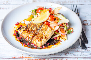 Grilled Barramundi with a side of salad, served on a white round plate with knife and fork.
