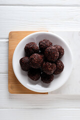 Brigadeiro in bowl on kitchen board on white wooden background, top view
