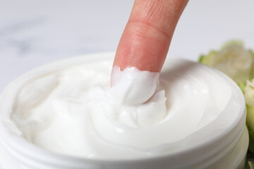 Jar with cream and finger on marble background, close up