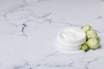 Jar with cream and roses on marble background, space for text