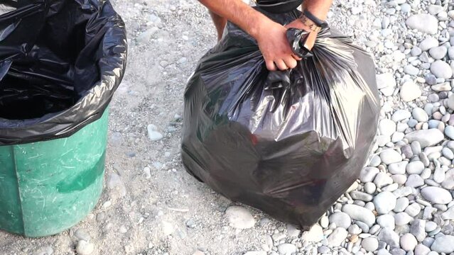 Garbage man on duty, collect garbage on beach. A janitor on the public beach takes a few big black bags of trash. Cleaner. Job. Working. Urban. Outdoor. Slow-motion, closeup, top aerial view