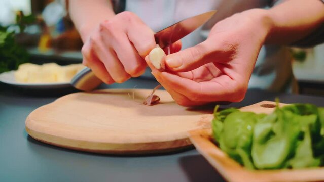 Woman peeling garlic with a knife on the kitchen table. Close-up of a table. Cooking in the kitchen.
