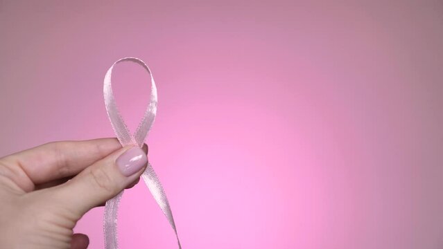 Pink symbolic ribbon in hands, symbol. World Breast Cancer Day. Close-up, isolated, pink neon background , professional lighting.