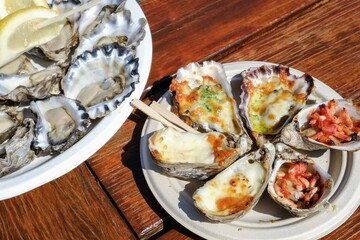 A plate of fresh Sydney rock oysters with lemon wedges and a smaller plate of grilled oysters with assorted toppings (garlic cheese, mornay, bacon) at Jim Wilds Oyster Shack, Greenwell Point, NSW