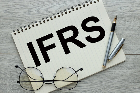International Financial Reporting Standards - blocks spelling IFRS. open notepad near glasses and a pen. text on the page