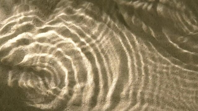 Close-up water surface ripples and splash, palm tree leaf shadow on sand texture