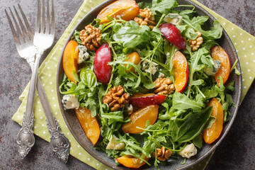 Vitamin breakfast salad of fresh plums, arugula, Gorgonzola cheese and walnuts close-up in a plate on the table. horizontal top view from above