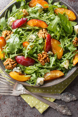 Fresh salad of plums, arugula, gorgonzola cheese and walnuts close-up in a plate on the table. Vertical top view from above