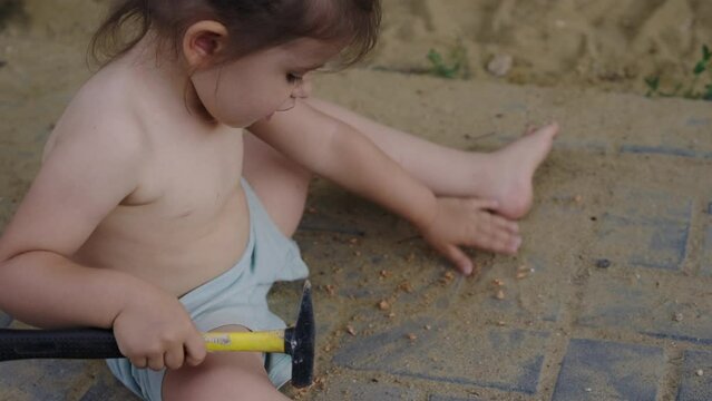 View of an atractive little baby girl playing with hammer toy in the garden. Positive child playing outdoor. People lifestyle portrait.