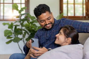 The triumph of a young Indian couple happily celebrates reading unexpected good news on their smartphone. young Indian couple together on the sofa in the living room