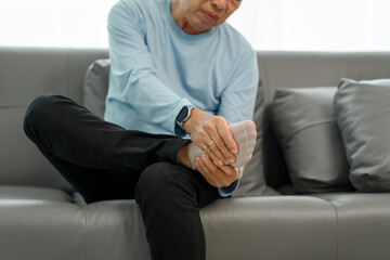 Senior Elderly Asian man in blue shirt suffering from intense foot and ankle pain on the sofa.