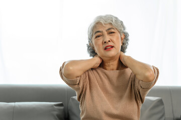 Elderly asian woman sitting on the couch, neck pain.