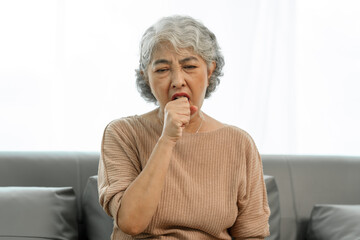 Elderly asian woman sitting on the couch, Cough, sore throat.