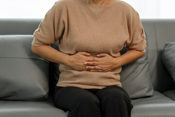 Elderly asian woman sitting on the couch, stomach ache.
