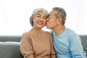 Affectionate senior Asian couple sharing warm embrace on the sofa, celebrating their enduring love and togetherness. Elderly husband and wife happy family