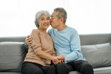 Affectionate senior Asian couple sharing warm embrace on the sofa, celebrating their enduring love and togetherness. Elderly husband and wife happy family