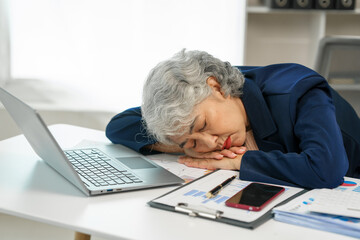 Mature businesswoman at her desk, overwhelmed by stress, feeling the weight of failure, and suffering from a headache, Stressful workday, Overwhelmed at work, Corporate crisis
