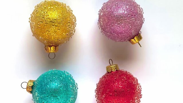 Yellow, pink, blue, and red Christmas ornaments spinning on a white background. Stop-motion animation