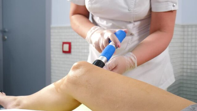 Therapist Doctor doing shock wave therapy on female Kknee in Modern Clinic. Physiotherapist Doctor performs Procedure on patient Feet. Rehabilitation, Patient getting Profilaxing Procedure of
