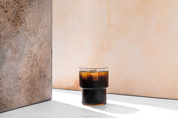 Refreshing iced  cold black coffee in a glass in a ray of light with copy space