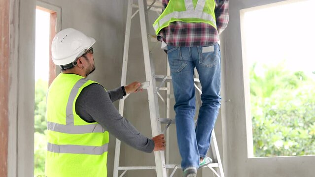 Safety working at workplace, Indian or Hispanic engineer or foreman climbing to house ceiling using water level meter equipment check incline degree, construction worker hold ladder to safe colleague