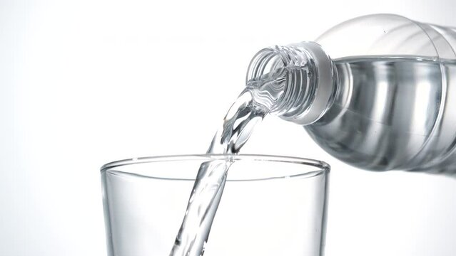 Pour bottled water into a clear glass placed on a white background.