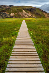 Fototapeta premium Landmannalaugar, Iceland. Camping site and mountain hut with a wooden path to bathing pool and beautiful Icelandic landscape of colorful rainbow volcanic Landmannalaugar mountains, 