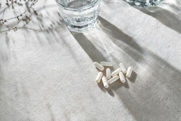 White capsules, glass with water and dried grass on neutral beige linen tablecloth with aesthetic...