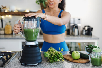 Latin fitness woman pouring green juice from mixer into glass in kitchen at home in Mexico Latin America, hispanic female on detox diet