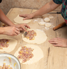 Women prepare pies from dough and minced meat on the table