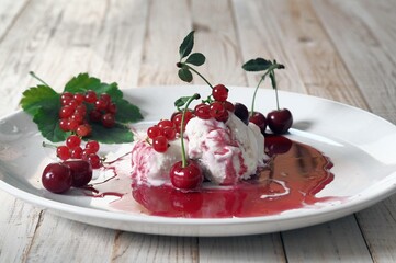 Red cherries and red currants on ice cream with jam in a white plate on a white wooden table.Food background.