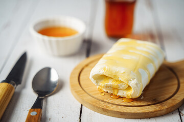 Close up picture of white cream milky kaymak butter roll poured with honey and tea on wooden plate.