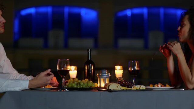 Young man and lady enjoying romantic dinner on the terrace in the evening outdoor while eating and talking. Romantic date on the roof. Romantic concept. Couple in love. Real time
