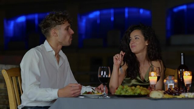 Smiling pretty lady feeding her boyfriend while having the date outdoor in the evening. Romantic date on the roof. Romantic concept. Couple in love. Real time