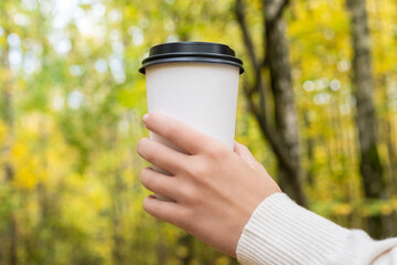 Woman hand with paper cup of coffee in autumn park