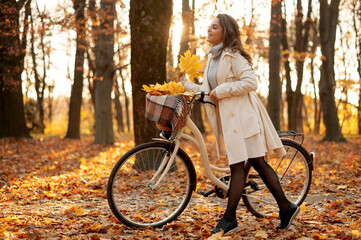 Beautiful happy woman in coat walking with bicycle in autumn park