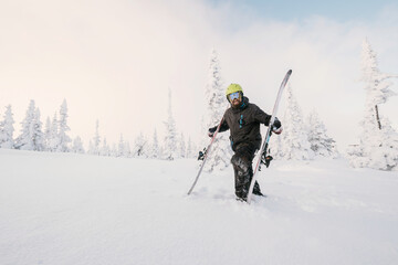 Male skier standing with skis on mountain meadow with snow-covered trees