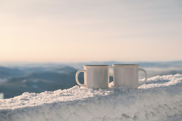 Hot drink in cups on frozen wooden table over winter mountains landscape