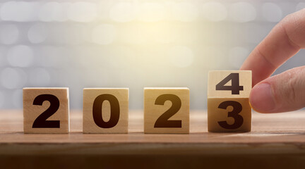 New year exchange concept. Man fingers with turning the calendar wooden block from 2023 to 2024....