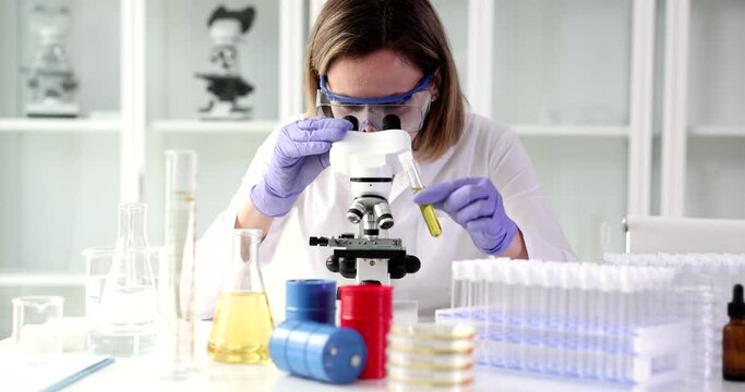 Examining oil sample under microscope. Laboratory scientist worker holding tube with oil in hand
