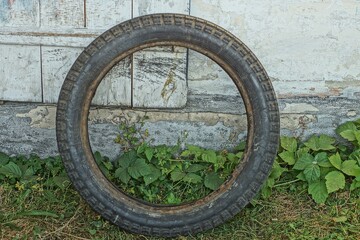 one old rubber round dirty tire from a motorcycle wheel stands on the ground near white wooden doors on the street during the day