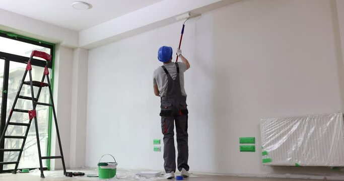 Painting gray wall white with paint roller. We make repairs in apartment room of house