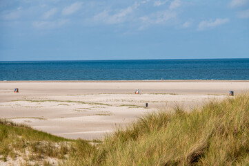 Fototapeta na wymiar Strandköbe auf einem leeren Sandstrand im Vordergrund eine Düne mit bilck über die Nordsee bis zum Horizont