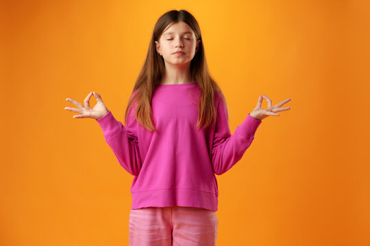 Teen girl standing in zen pose against yellow background