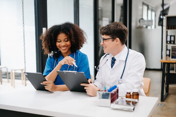 Focused mature male doctor and African female nurse look at tablet and laptop discuss anamnesis together. Concentrated diverse medical professionals in hospital.