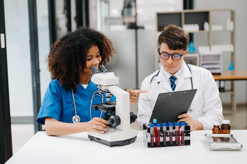 Focused mature male doctor and African female nurse look at tablet and laptop discuss anamnesis together. Concentrated diverse medical professionals in hospital.